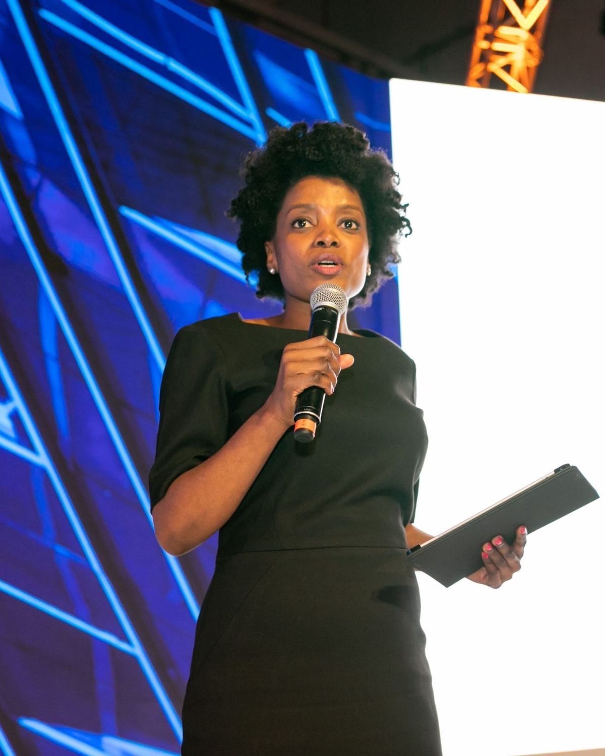 Maud Nale on stage, speaking into a handheld microphone